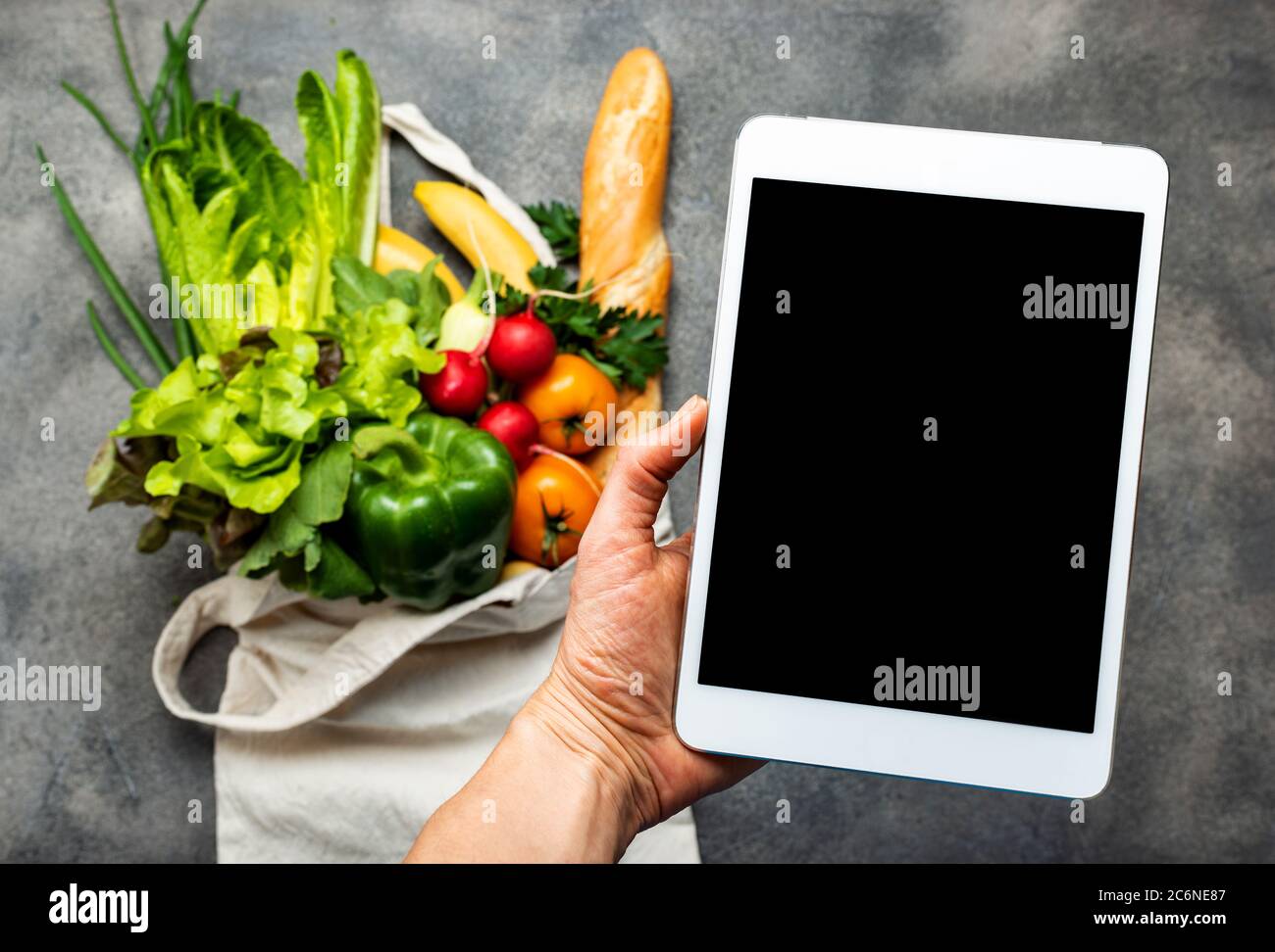 Tablette avec écran vierge dans la main féminine au-dessus du sac d'achats plein de nourriture saine. Commander des aliments livrés en ligne. Banque D'Images