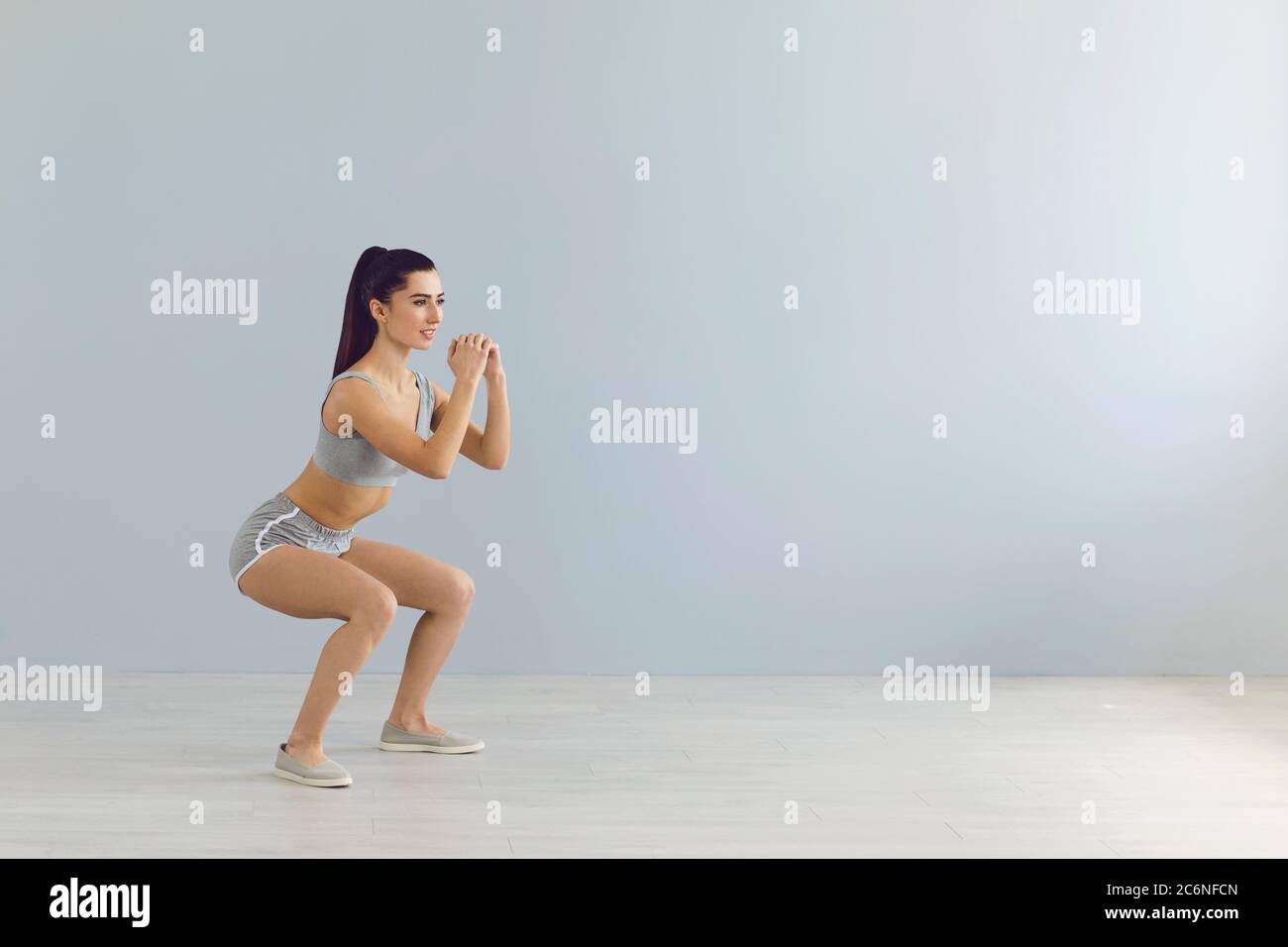 Ajuster la sportswoman faisant des squats pendant l'entraînement près du mur Banque D'Images