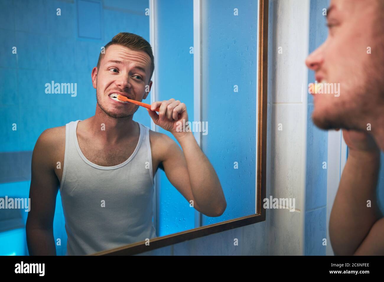 Routine d'hygiène du matin. Homme se brossant les dents et regardant dans le miroir de la salle de bains de la maison. Banque D'Images