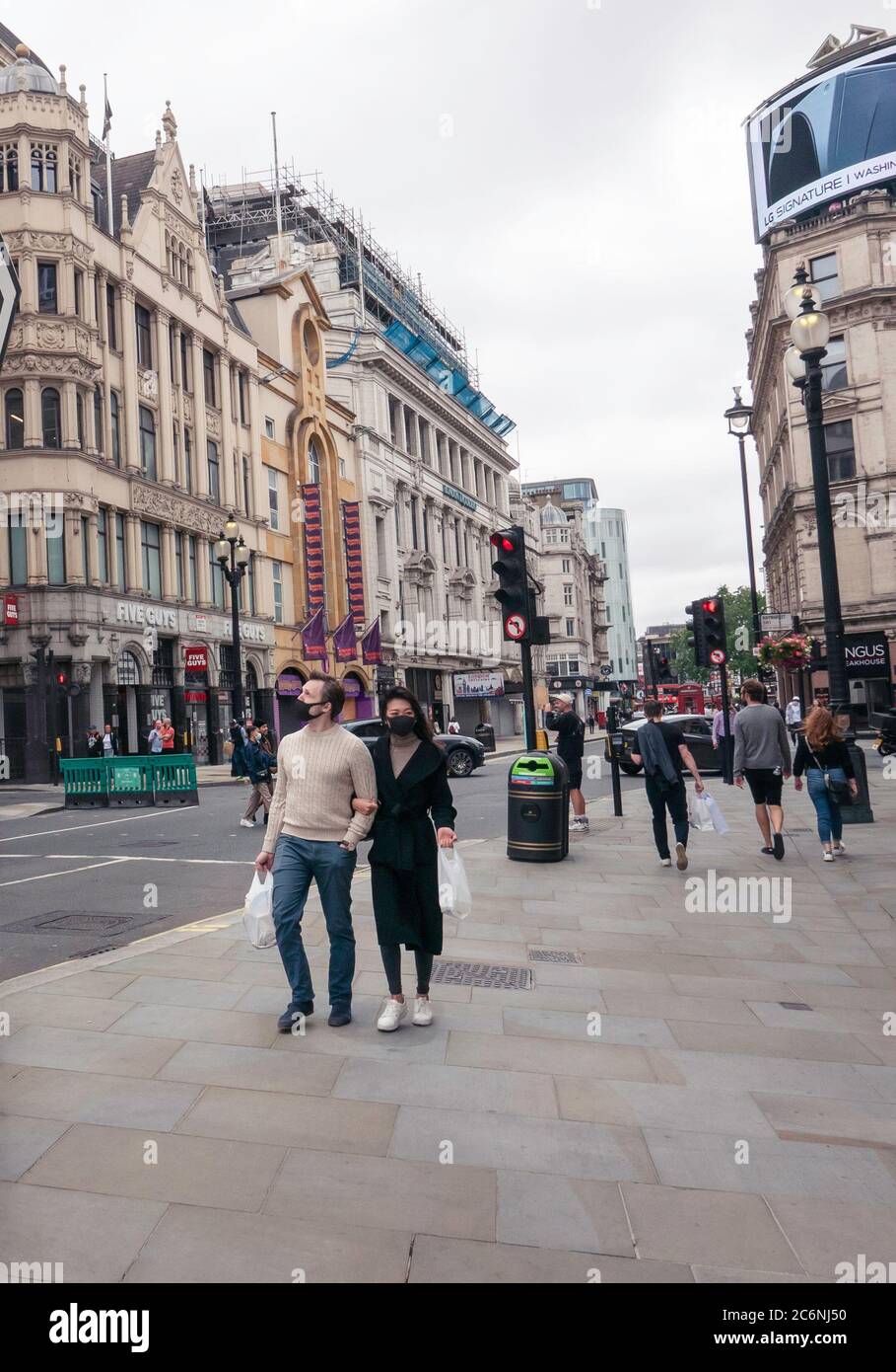 Homme et femme avec des couvre-visage à Piccadilly Circus pendant la pandémie de Covid-19. Banque D'Images