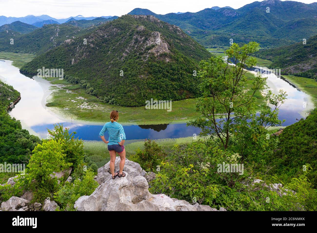 Femme debout sur un rocher au-dessus de la courbe de la rivière Rijeka Crnojevica, vue du point de vue de Pavlova strana, près de Cetinje Banque D'Images