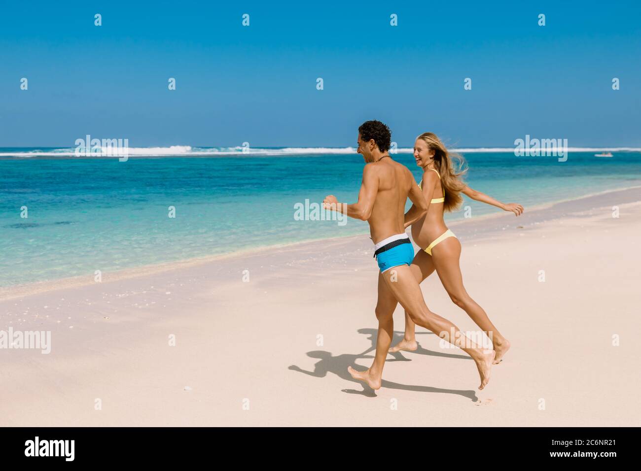 Couple de course à pied heureux. Femme enceinte avec mari s'attendant à bébé à la plage tropicale avec mer bleue Banque D'Images