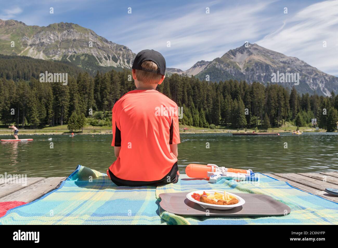 garçon assis sur une promenade en bois et regardant sur un lac Banque D'Images