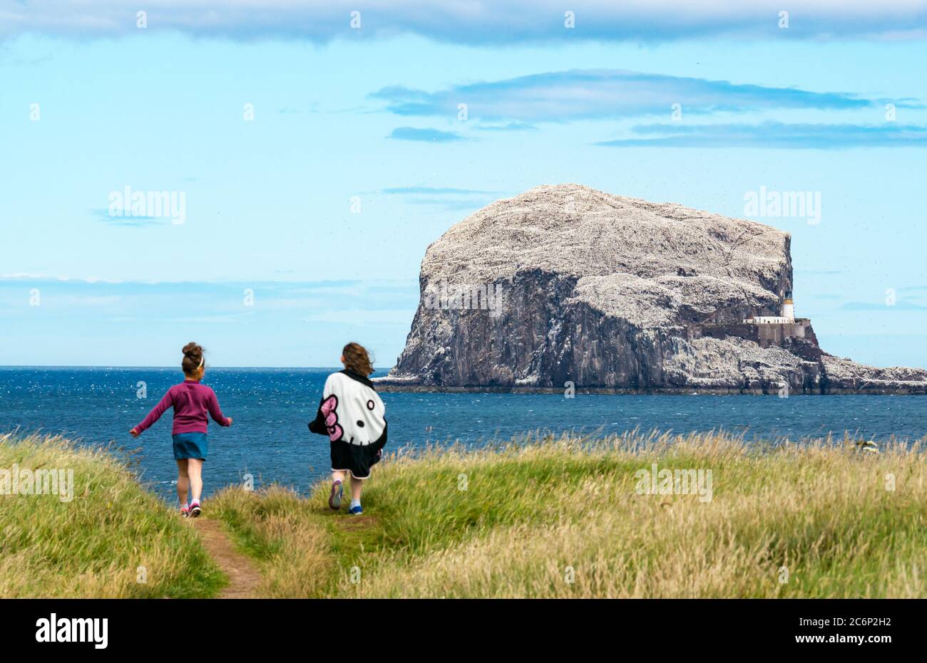 North Berwick, East Lothian, Écosse, Royaume-Uni, 11 juillet 2020. Météo britannique : une journée ensoleillée très tranquille dans la ville côtière le long de la rive du Firth of Forth. La colonie de gannet de Bass Rock est éclairée au soleil tandis que deux jeunes filles marchent sur le sentier côtier de falaise Banque D'Images