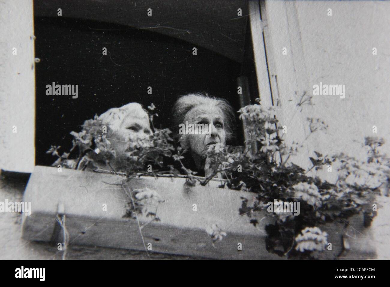 Fin 70s vintage noir et blanc de style de vie photographie de deux femmes âgées regardant par leur fenêtre et commettant des potins sur les gens. Banque D'Images