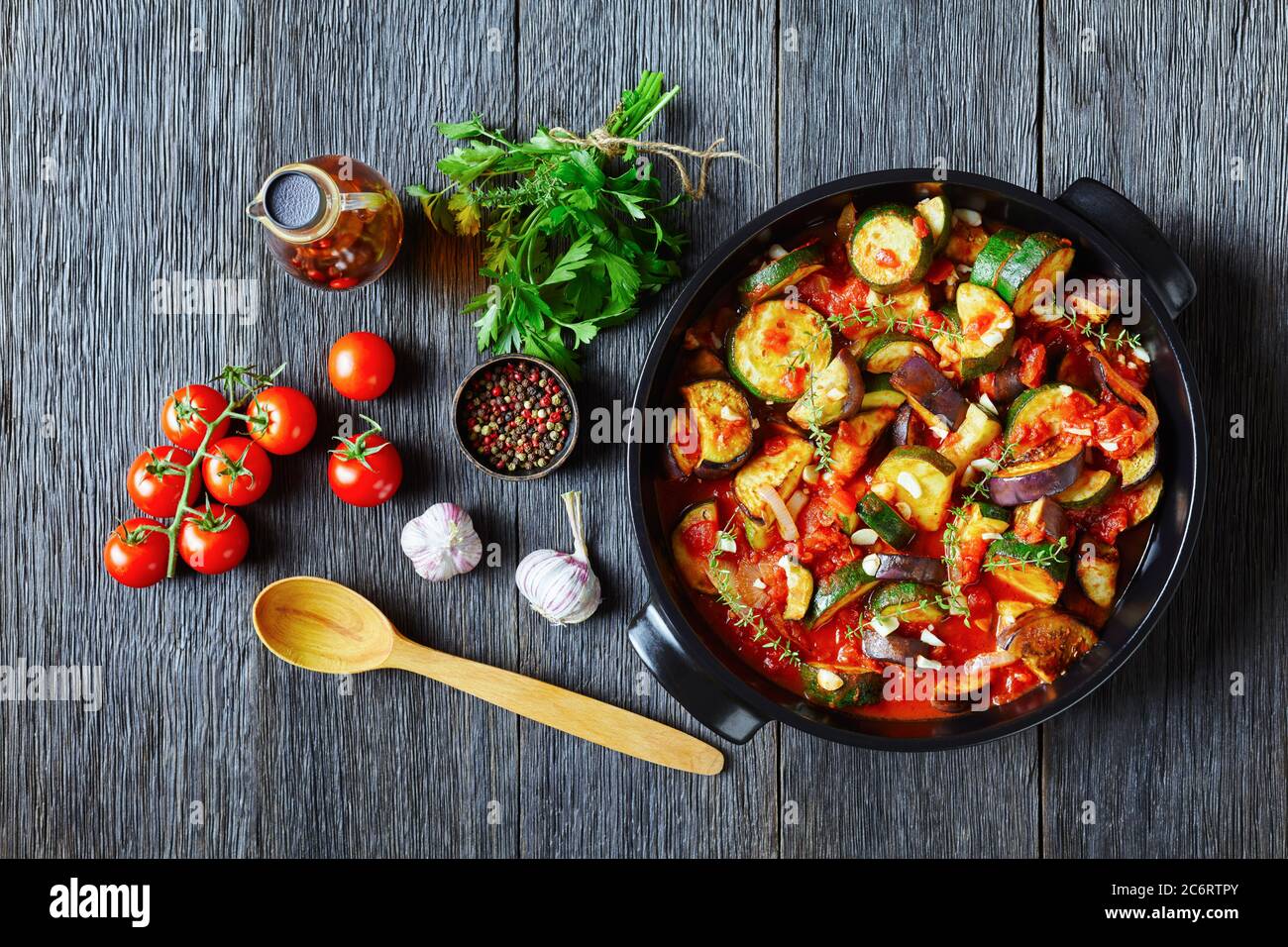 ragoût de légumes, aubergine, oignon, courgettes avec sauce tomate, ail et herbes dans un plat de cuisson sur une table en bois avec des ingrédients, vue sur le paysage de Banque D'Images