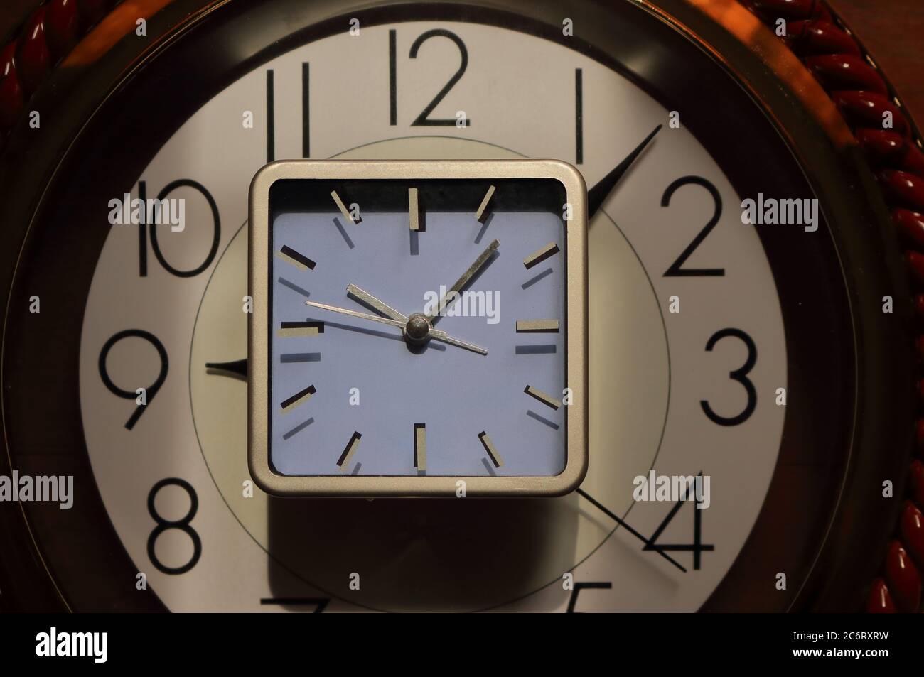 Mise au point sélective sur les aiguilles d'horloge de petite horloge rectangulaire placée sur une grande horloge ronde, métaphore de concept temps après temps Banque D'Images
