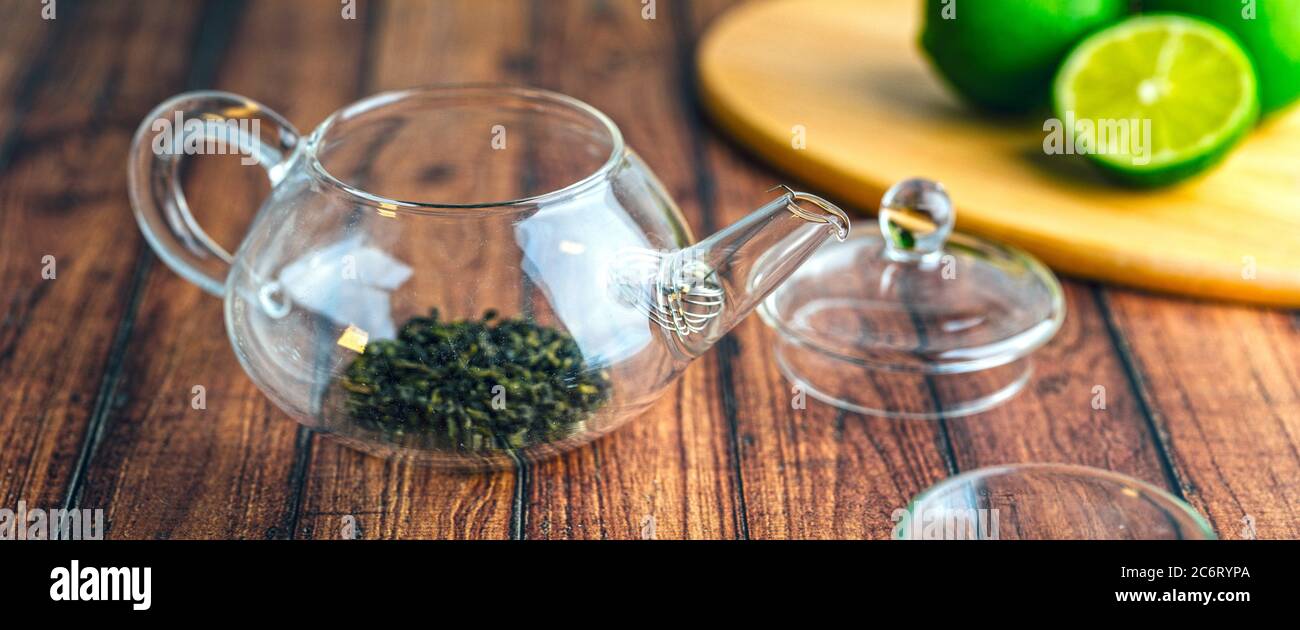 Une théière en verre avec des feuilles de thé à l'intérieur sur une table en bois. Banque D'Images