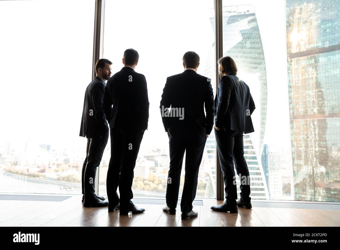 De jeunes hommes d'affaires prospères discutent de questions de travail près de la fenêtre panoramique. Banque D'Images