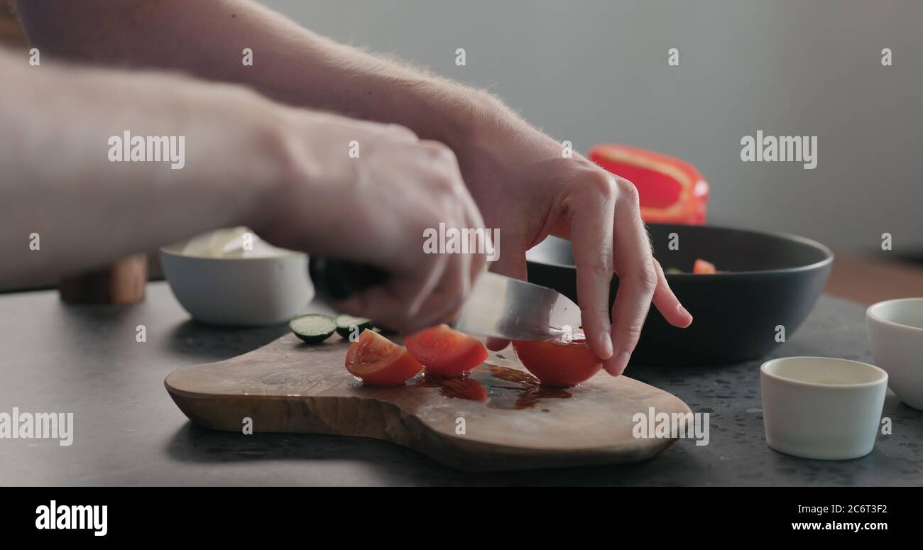 l'homme hache les tomates sur une planche à bois d'olive Banque D'Images