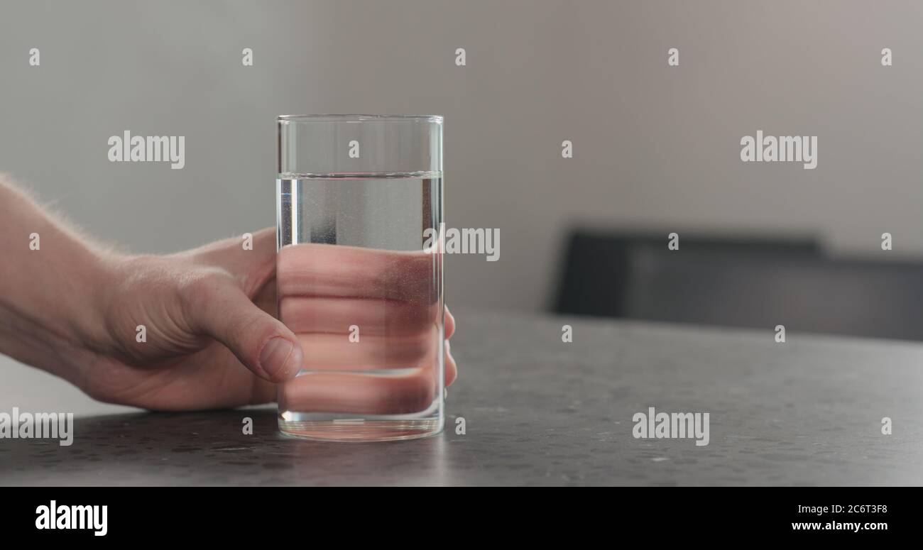 homme main prend un verre d'eau de plan de travail en béton Banque D'Images