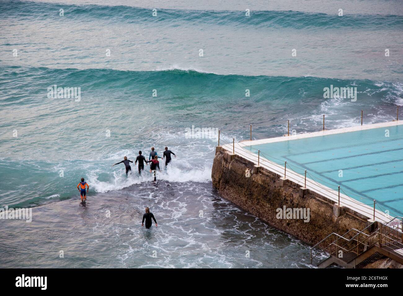 Les nageurs en combinaison jouent sur les vagues près de la piscine sur la plage de Bondi Banque D'Images