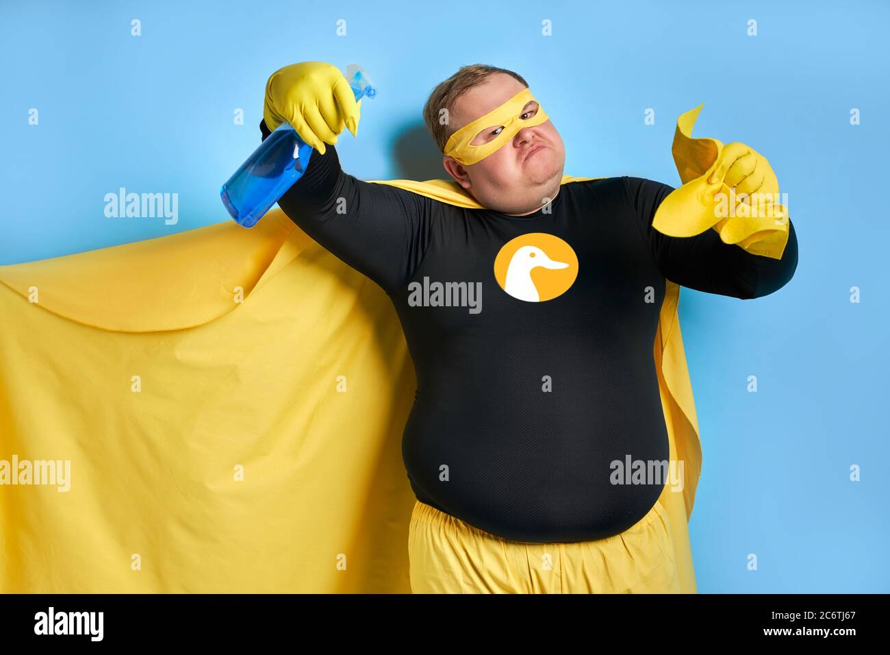 portrait de drôle gai gras homme avec détergent dans les mains, l'homme est prêt à nettoyer, portant le costume jaune, les gants et le masque de super-héros. isolé bleu Banque D'Images