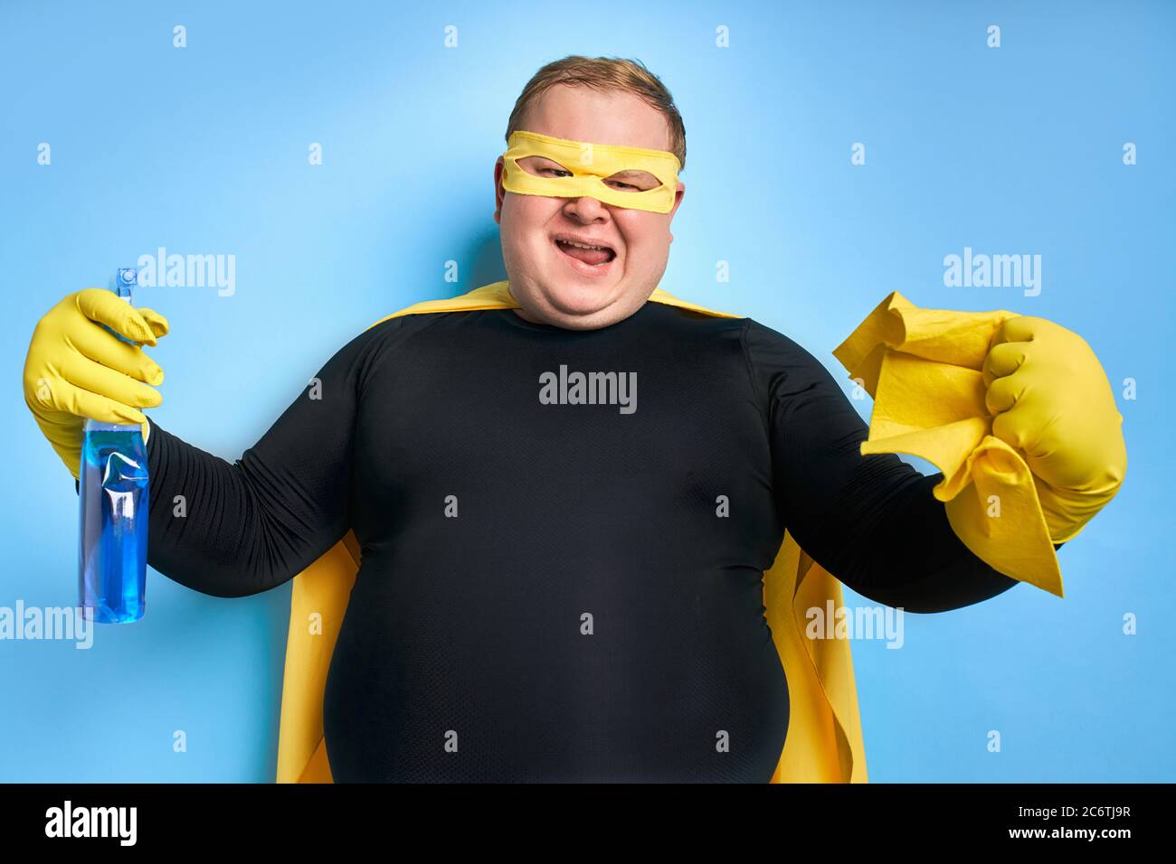 portrait de drôle gai gras homme avec détergent dans les mains, l'homme est prêt à nettoyer, portant le costume jaune, les gants et le masque de super-héros. isolé bleu Banque D'Images