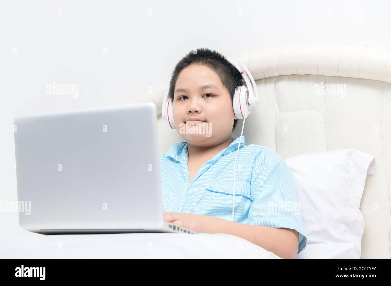 Obèse élève assis et porter des écouteurs pour apprendre en ligne à partir d'un ordinateur portable sur leur lit à la maison. Épidémie de coronavirus. Fermeture des écoles et des établissements d'enseignement. CO Banque D'Images