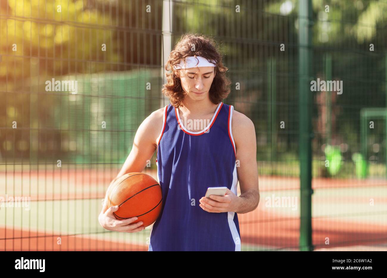 Joueur de basket-ball millénaire sérieux utilisant un smartphone sur un terrain extérieur après le match Banque D'Images