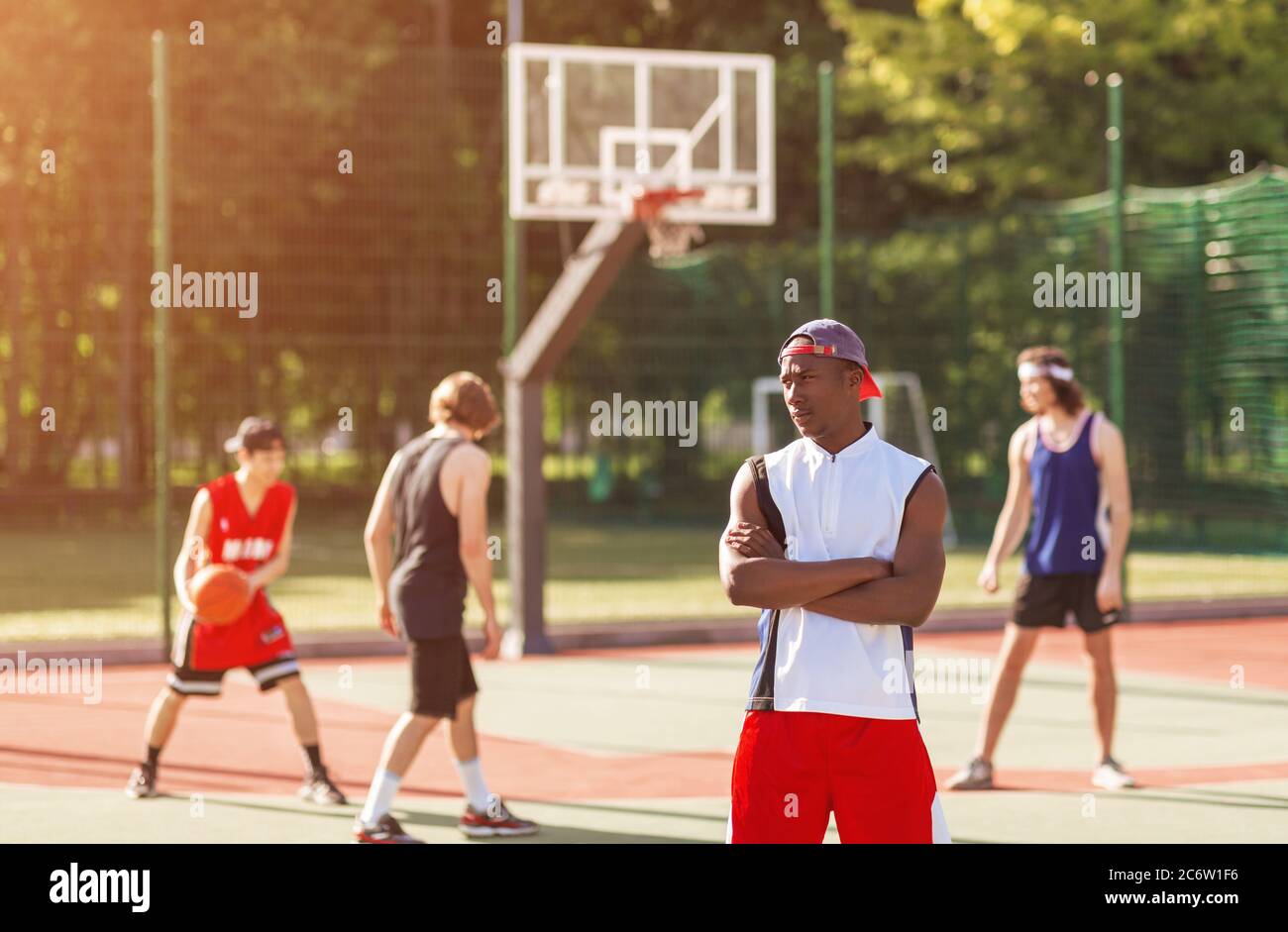 Un joueur de basket-ball afro-américain avec une équipe diversifiée debout sur un terrain de jeu extérieur, dans un espace vierge Banque D'Images