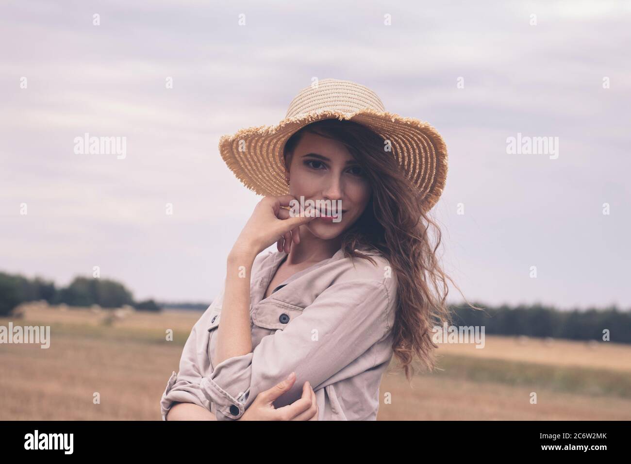 Une jeune fille attrayante dans un chapeau de paille se tient dans un champ. Femme aime les loisirs en plein air. Banque D'Images