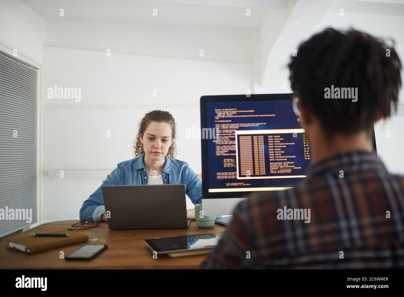 Vue arrière portrait de l'homme afro-américain écrivant du code sur l'écran d'ordinateur tout en travaillant à un bureau dans l'agence de développement de logiciels avec une collègue féminine Banque D'Images