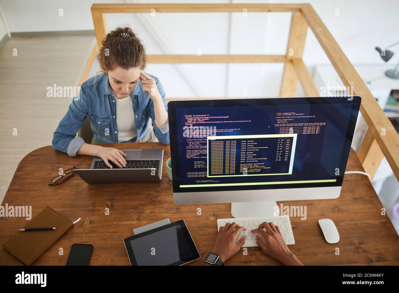 Portrait en grand angle d'une jeune femme utilisant un ordinateur portable tout en travaillant au bureau dans une agence de développement de logiciels avec un collègue mâle méconnaissable écrivant le code o Banque D'Images