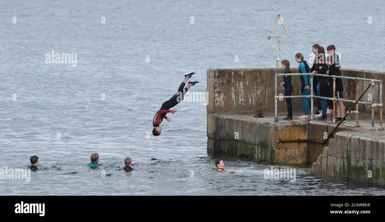 Un groupe de jeunes sautent dans le port de la baie Rouge à Cusendall, Co Antrim, alors que les températures montent à 22 degrés Celsius. Banque D'Images