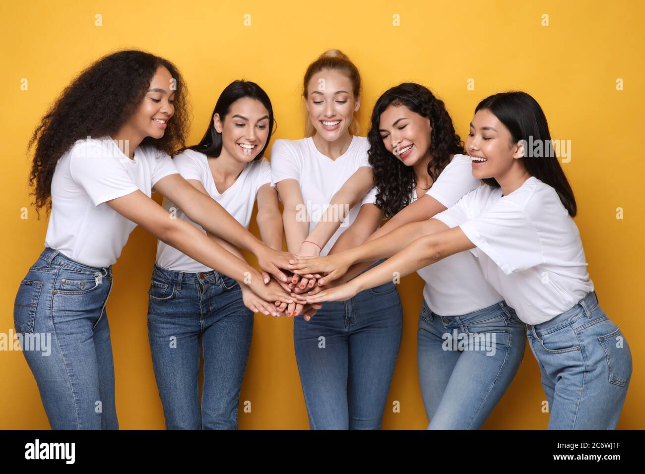 Filles positives tenant les mains debout sur fond de studio jaune Banque D'Images