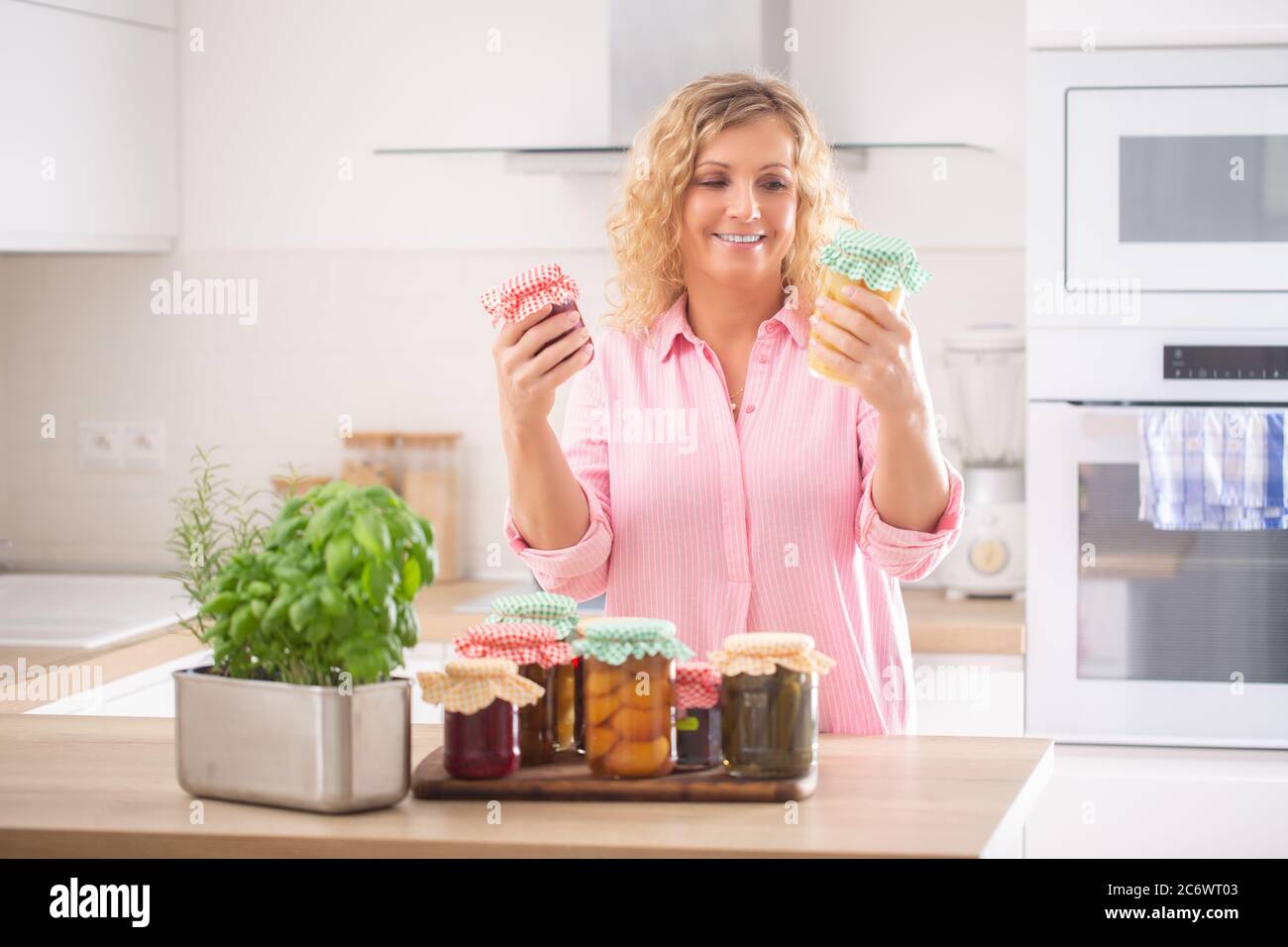 Femme regardant des conserves maison fraîches dans ses mains avec plus de cornichons dans des pots en face d'elle. Banque D'Images