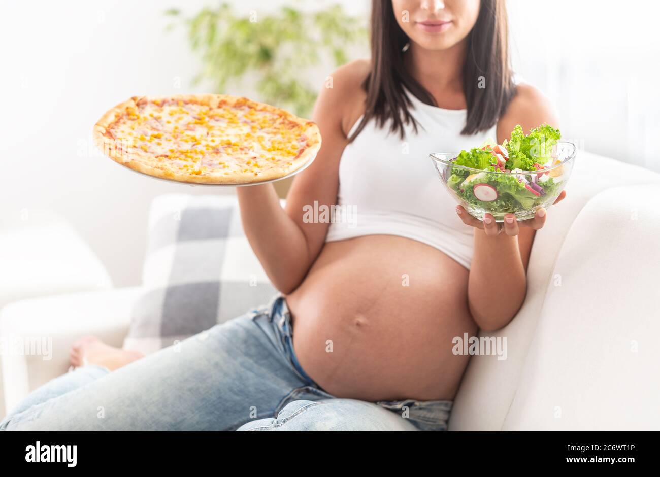 Fille enceinte assise sur un canapé tenant un saladier dans une main et une  pizza dans l'autre Photo Stock - Alamy