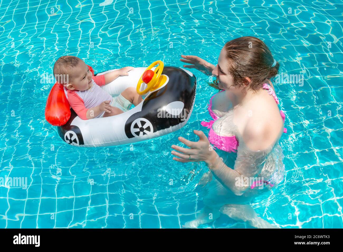 Jeune Mere Heureuse Dans Un Bikini Rose Ayant Le Plaisir Et Attrape Bebe Dans La Piscine Un Petit Enfant Joyeux S Assoit Dans Un Bateau Gonflable En Forme De Voiture Loisirs D Ete En