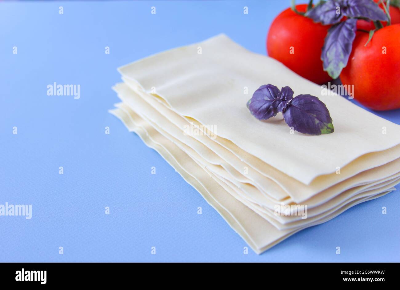 Feuilles de lasagne pâtes avec feuilles de tomate et de basilic sur fond bleu. Ingrédients pour une recette italienne. Copier l'espace. Banque D'Images