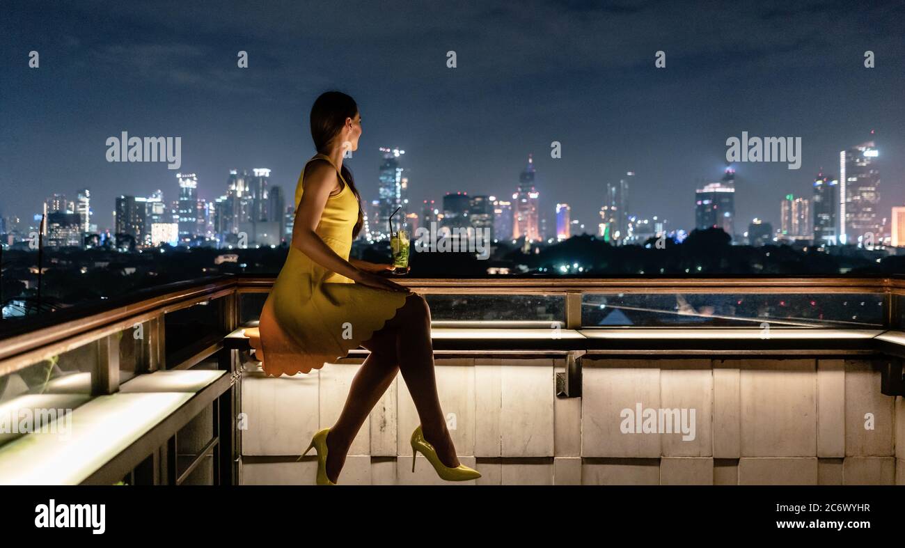 Femme prenant un verre sur la terrasse du toit donnant sur la ville Banque D'Images