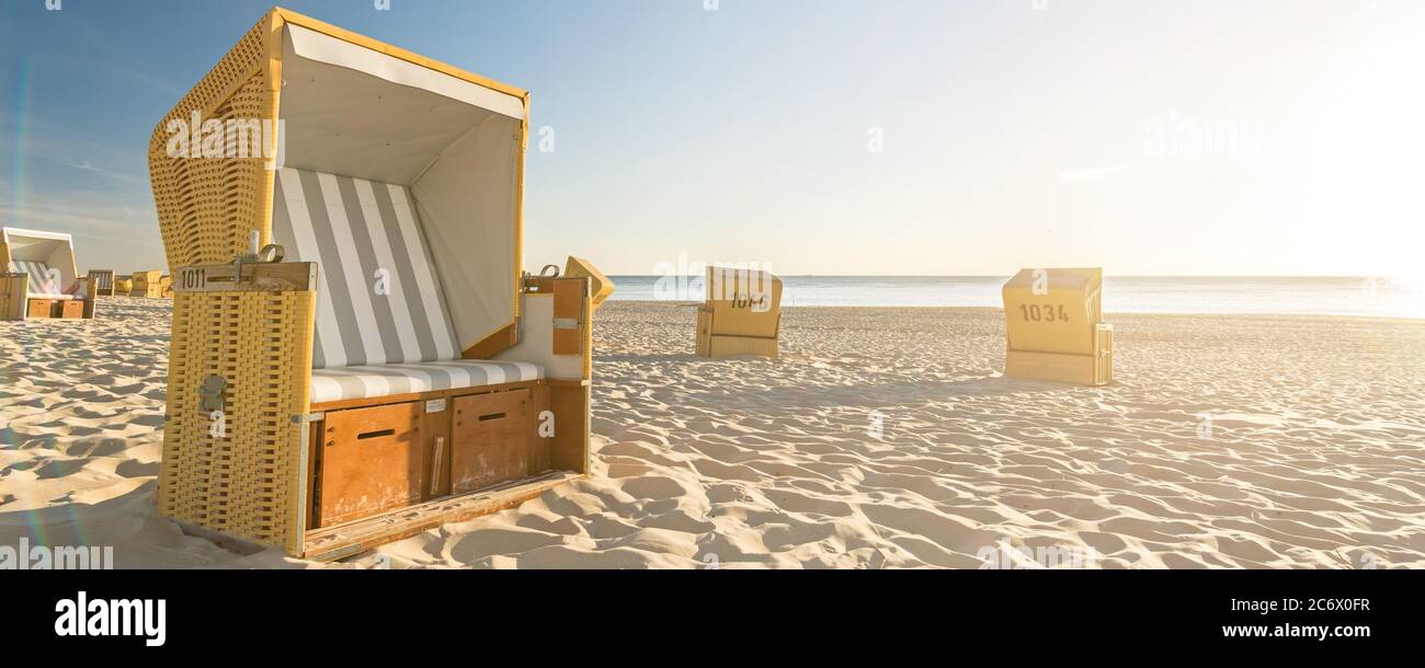 Chaises de plage à l'océan avec des reflets panoramiques de lentille pendant le coucher du soleil sur l'île de Sylt en Allemagne (format bannière) Banque D'Images