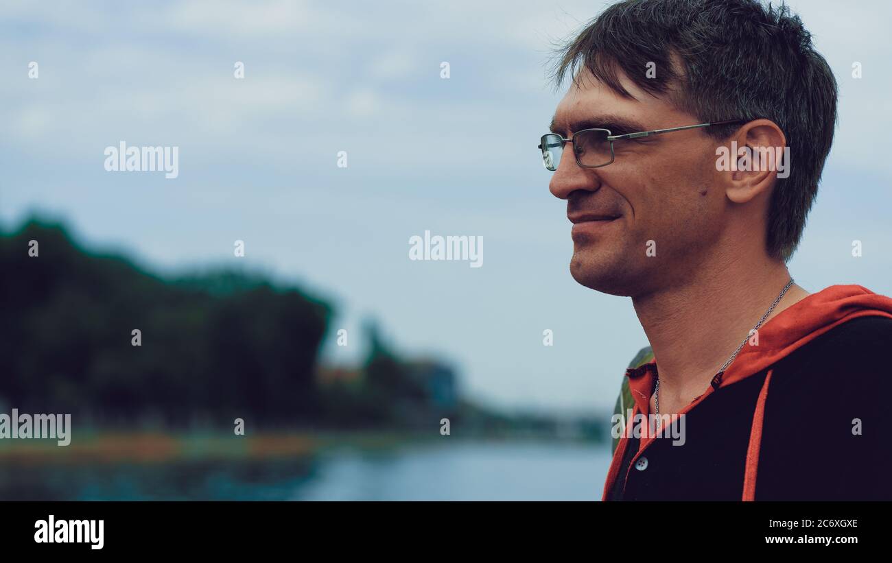Homme mûr avec des lunettes debout sur un remblai. Homme adulte appréciant une promenade dans la ville. Banque D'Images