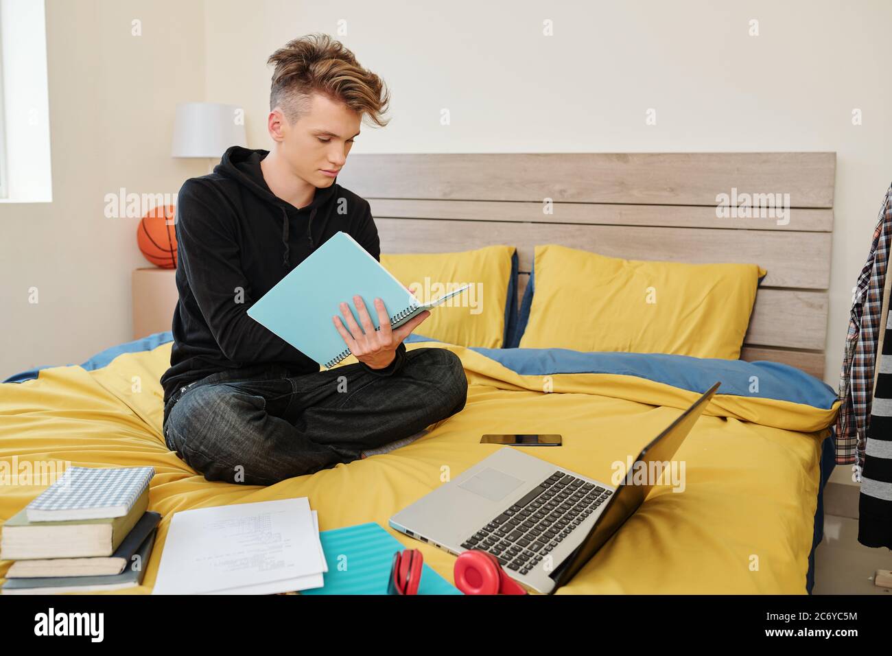 Étudiant en génie logiciel assis sur le lit avec des livres, ordinateur portable et manuels et écrire dans un bloc-notes Banque D'Images