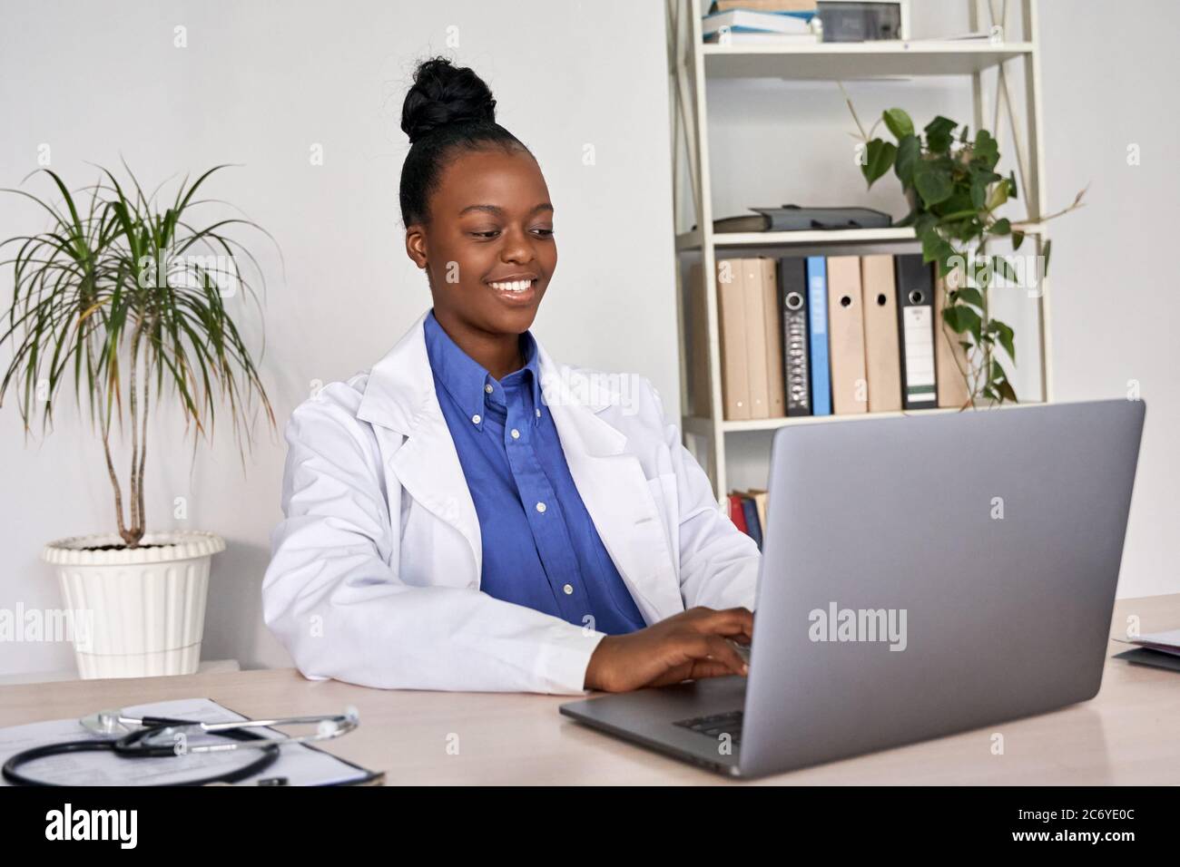 Souriant, femme africaine médecin généraliste américaine utilisant un ordinateur portable sur le lieu de travail. Banque D'Images