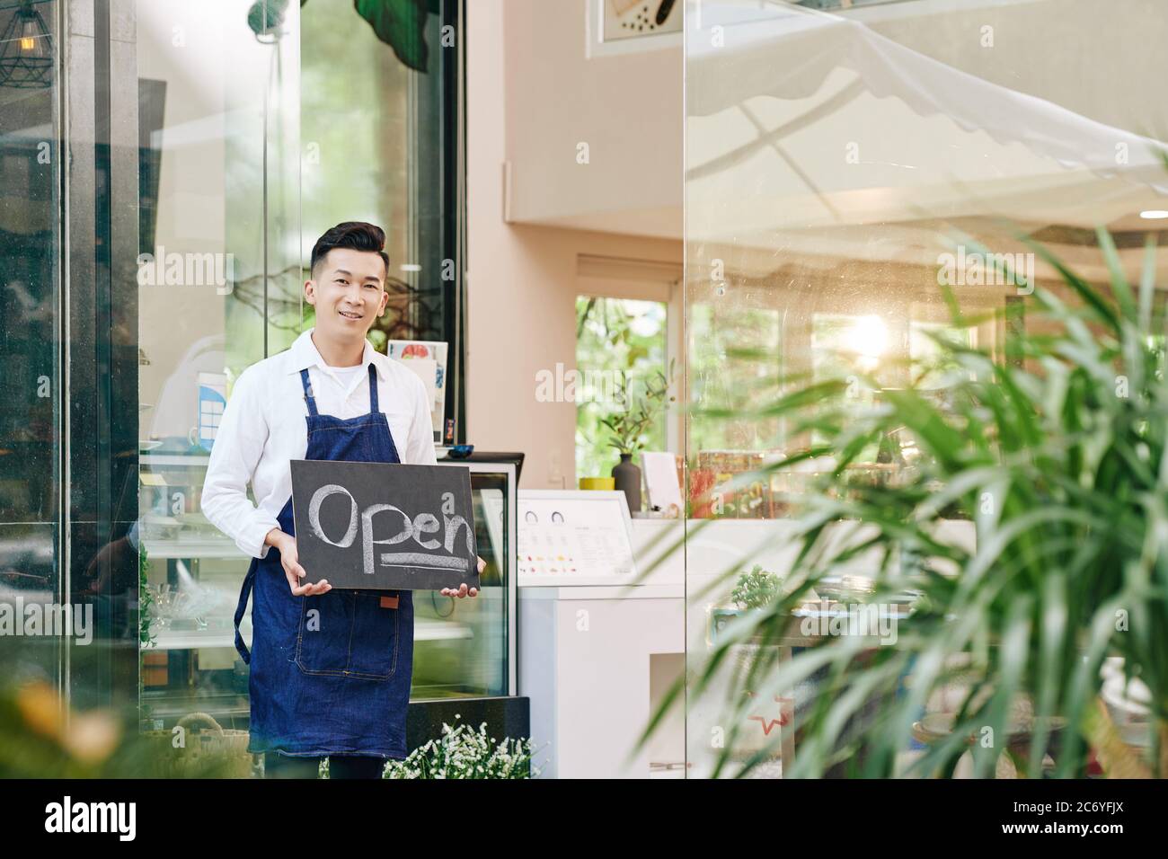 Un serveur souriant et heureux se tient à l'entrée et affiche une affiche ouverte lorsque les clients sont accueillis après le verrouillage Banque D'Images