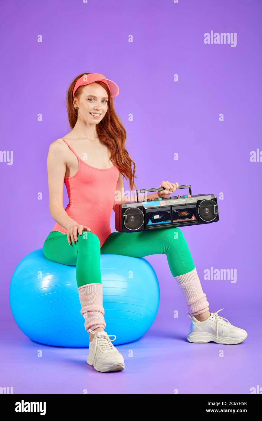 elle est assise sur un ballon de fitness avec un lecteur de cassettes  portable sur ses genoux, attendant que son professeur de danse commence la  leçon de danse, vêtu d'un élégant body