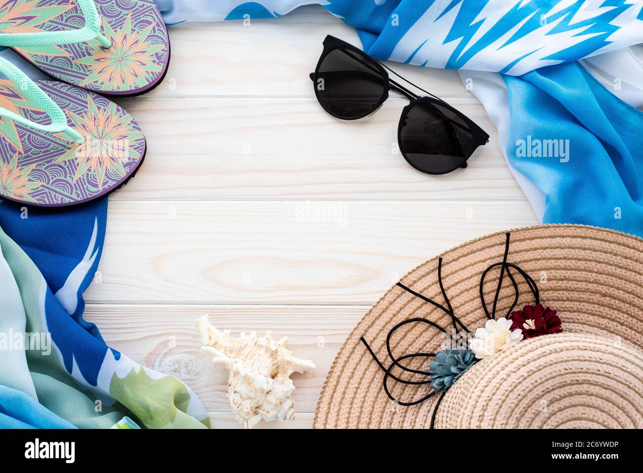 Accessoires de plage d'été. Tongs colorées, coque, lunettes de soleil noires, paréo bleu et chapeau de paille sur fond de bois. Le concept de vacances en mer, le Banque D'Images