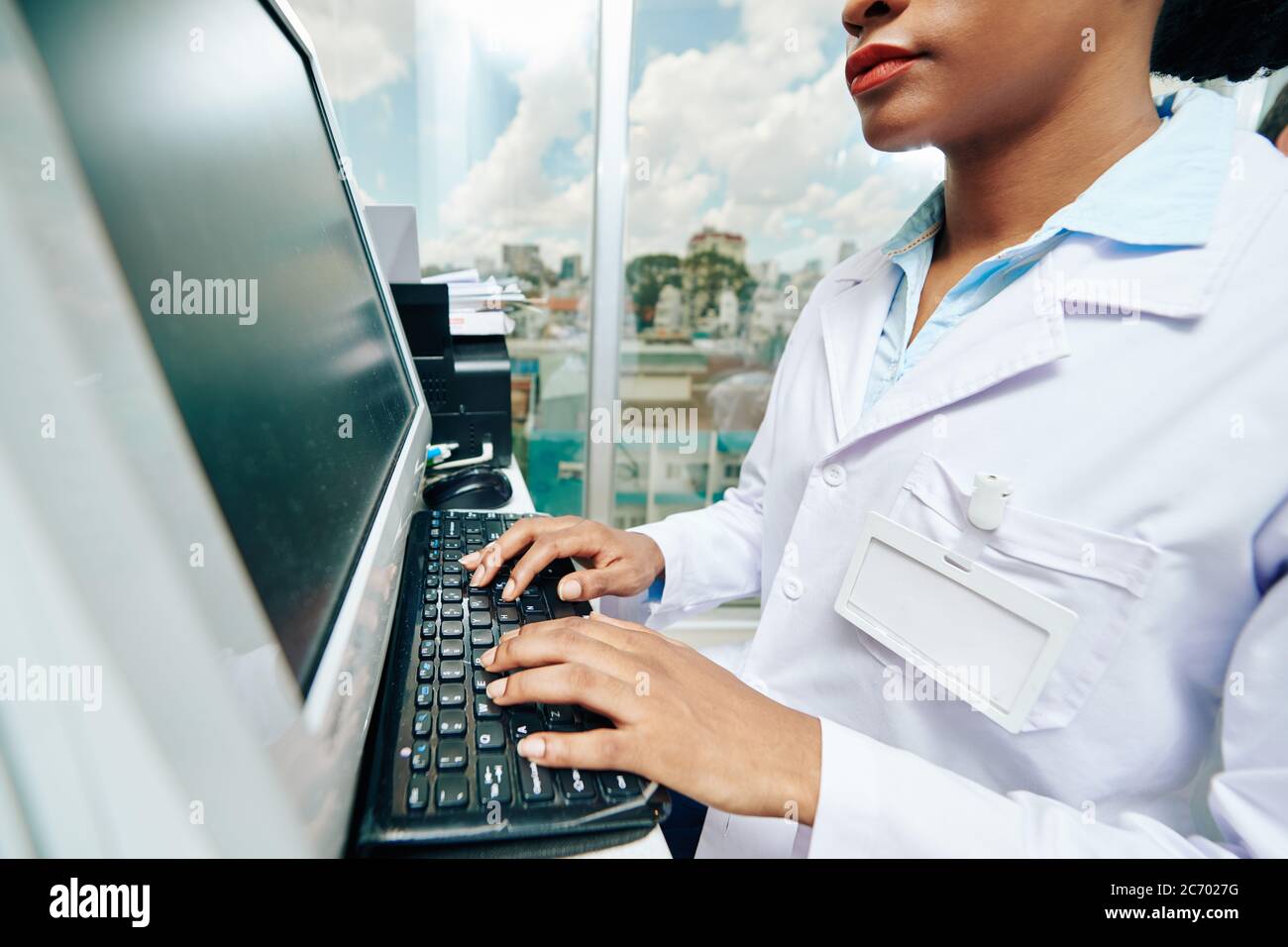 Image rognée d'une jeune femme noire sérieuse médecin travaillant sur ordinateur en clinique et vérifiant les documents du patient Banque D'Images