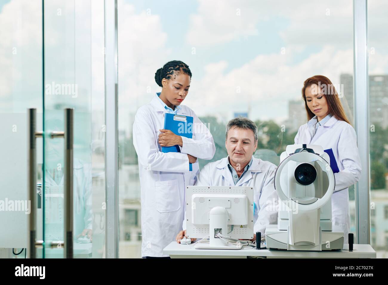 Un médecin mûr souriant montrant les résultats du test médical aux jeunes femmes internes et leur demandant de diagnostiquer la maladie Banque D'Images