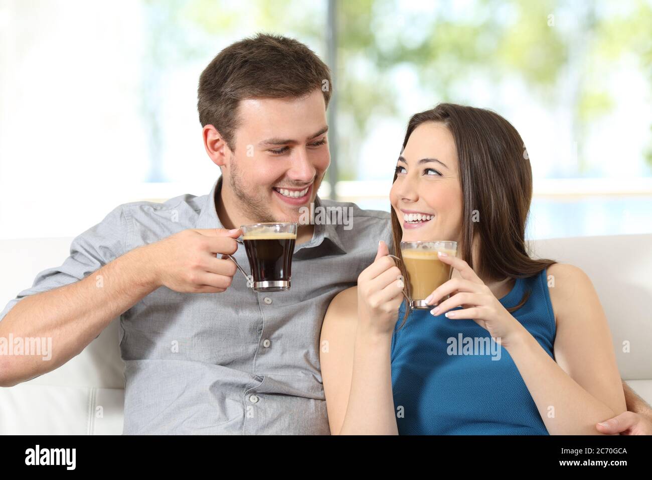 Couple heureux avec des tasses de café regardant l'un l'autre assis dans le canapé à la maison Banque D'Images