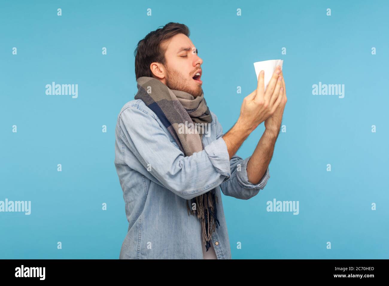 Portrait d'un homme malade de la grippe debout enveloppé de toux chaude de foulard, éternuant dans une serviette, se sentant mal souffrir de symptômes de grippe saisonnière, allergie Banque D'Images