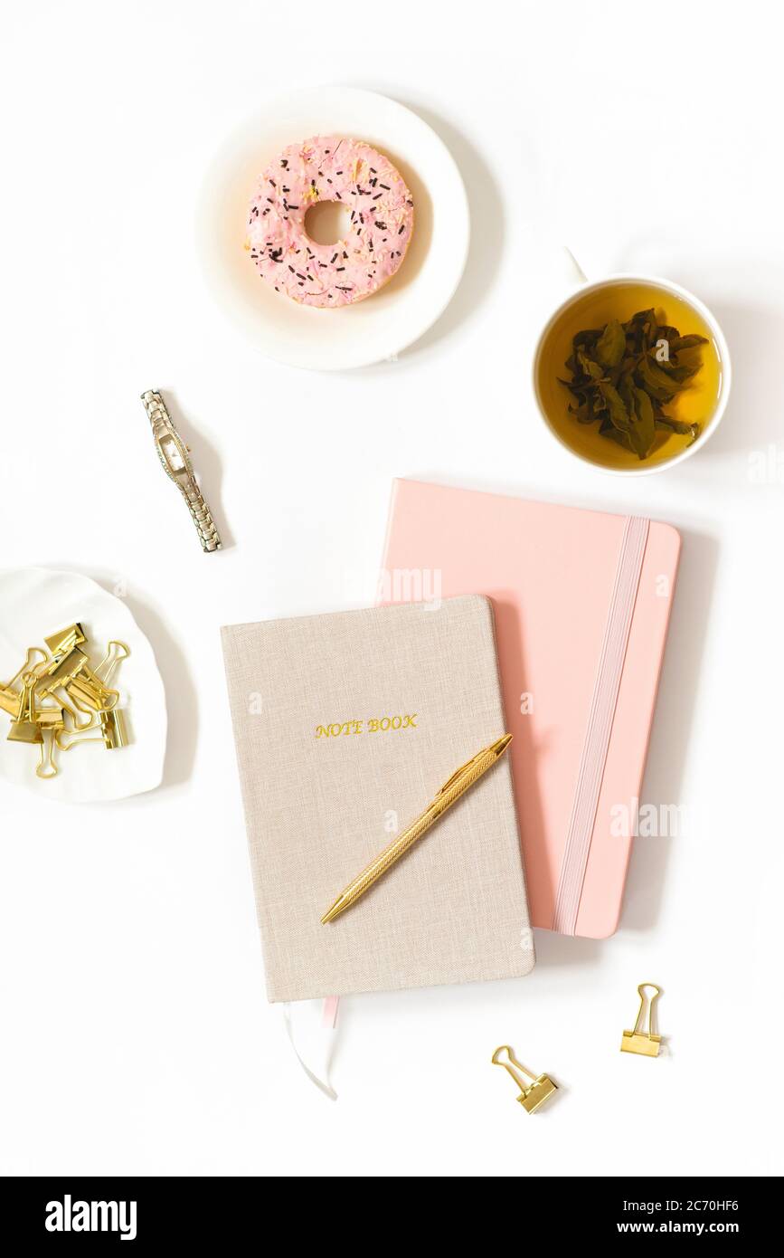 Pause thé sur le lieu de travail d'une freelance ou d'une femme blogger. Donat, thé dans une tasse, carnets, stylo sur fond blanc. Tendance de fond pour le blog Banque D'Images