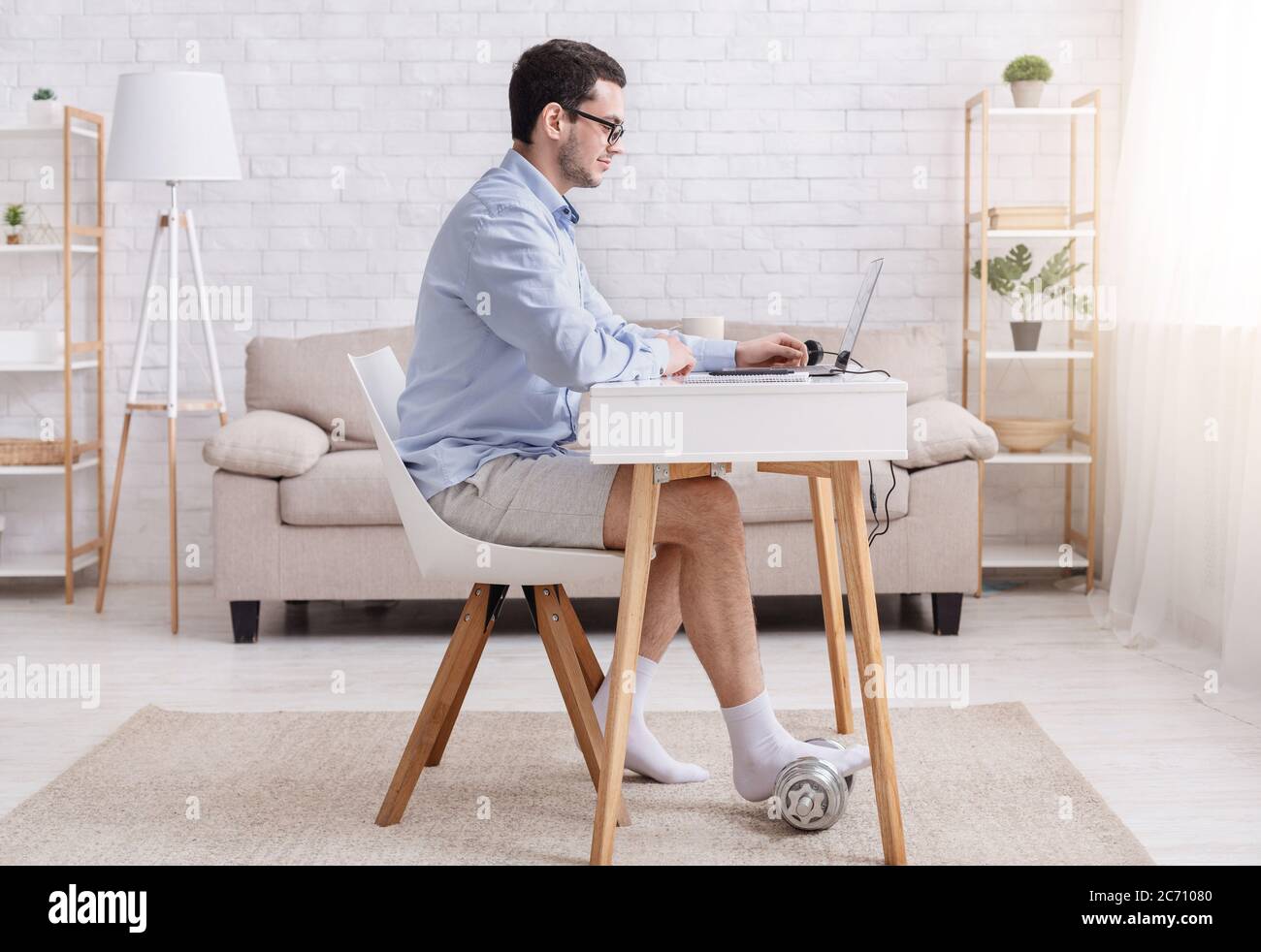 Sport, visioconférence et travail à domicile. Homme d'affaires en chemise et short, assis à table et à discuter, mettre le pied sur la haltère Banque D'Images