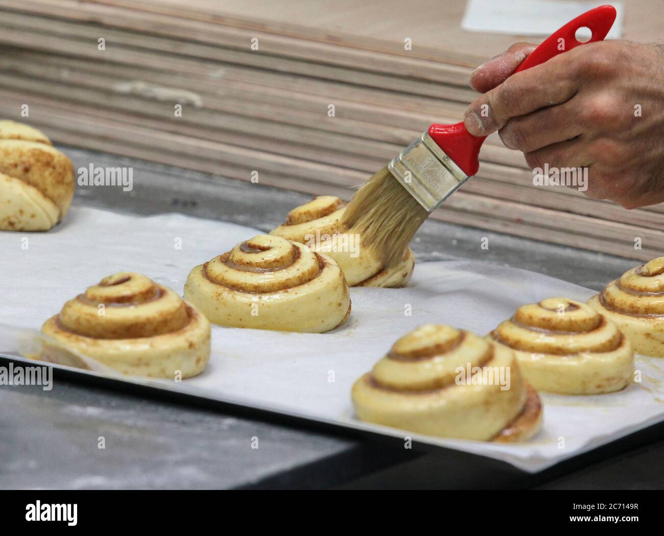 Les petits pains à la cannelle en forme sont autorisés à léaven avant de cuire, tandis que le glaçage aux œufs est brossé. Photographié dans une boulangerie Banque D'Images