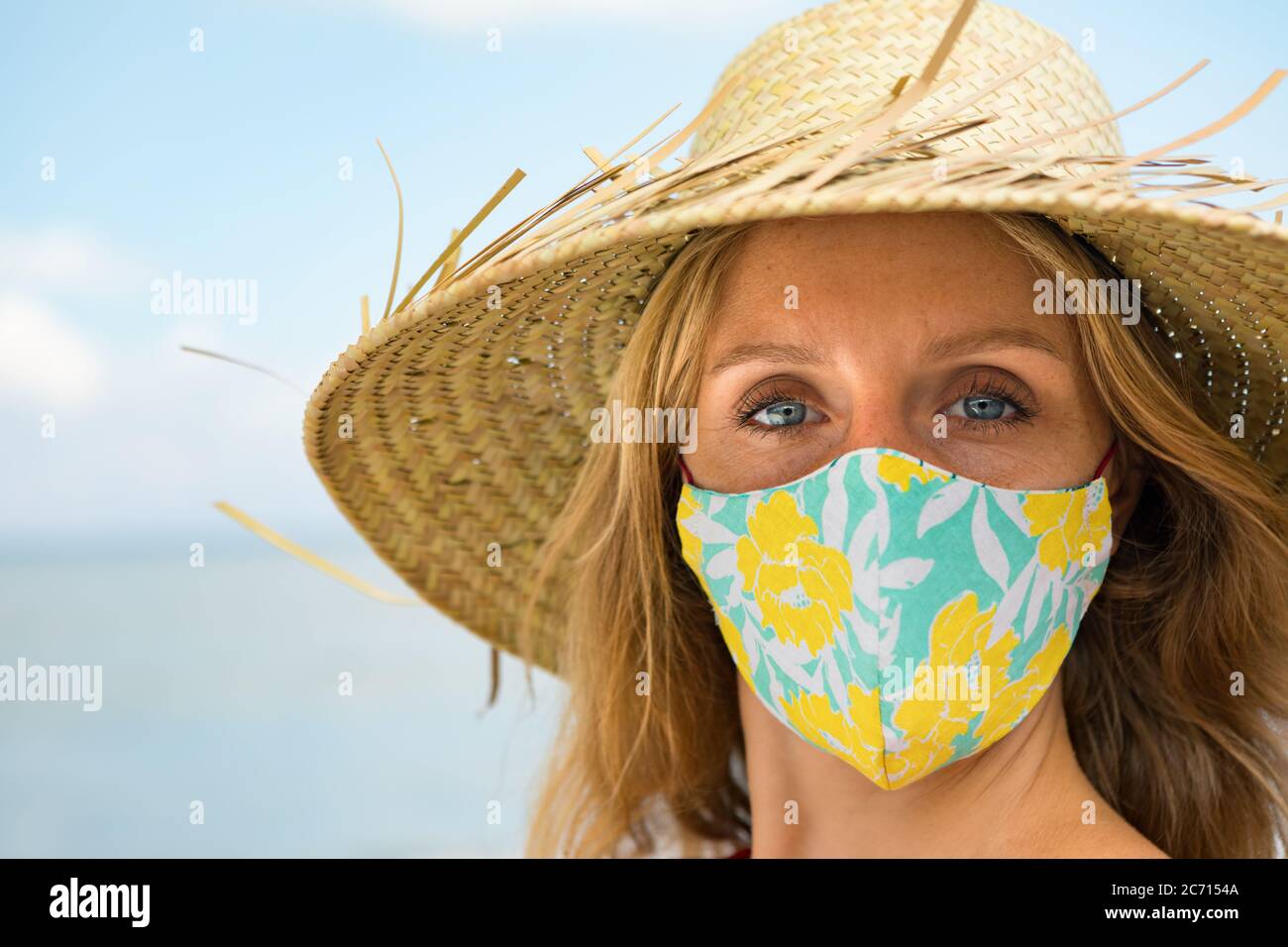 Portrait drôle de la jeune femme en chapeau de paille sur la plage tropicale de mer. Nouvelles règles pour porter un masque de couverture en tissu dans les lieux publics en raison du coronavirus COVID 19 Banque D'Images
