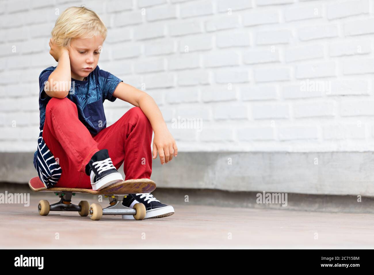 Le patineur qui a l'air malheureux et contrarié s'assoit sur le skateboard avant que les enfants s'entraîne dans le parc de skate. Vie familiale active, activités de loisirs en plein air Banque D'Images