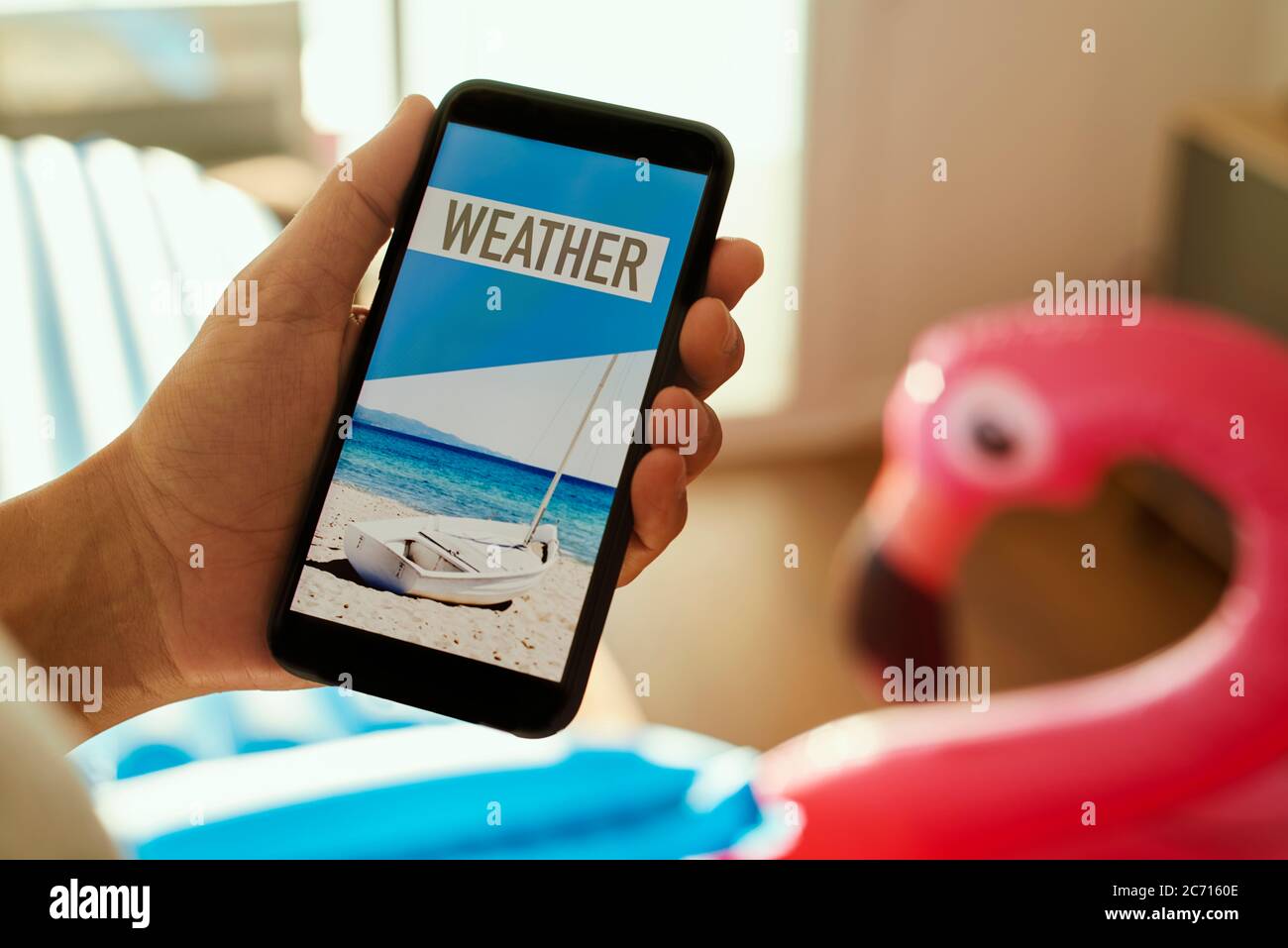 gros plan d'un jeune homme, portant des vêtements d'été décontractés, assis sur un fauteuil, ayant son smartphone dans les mains avec le texte météo dans son écran, Banque D'Images