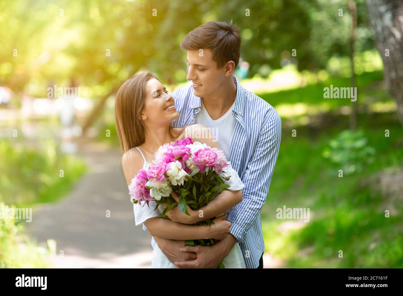 Jeune mari et femme avec bouquet de fleurs célébrant l'anniversaire à l'extérieur le jour d'été Banque D'Images