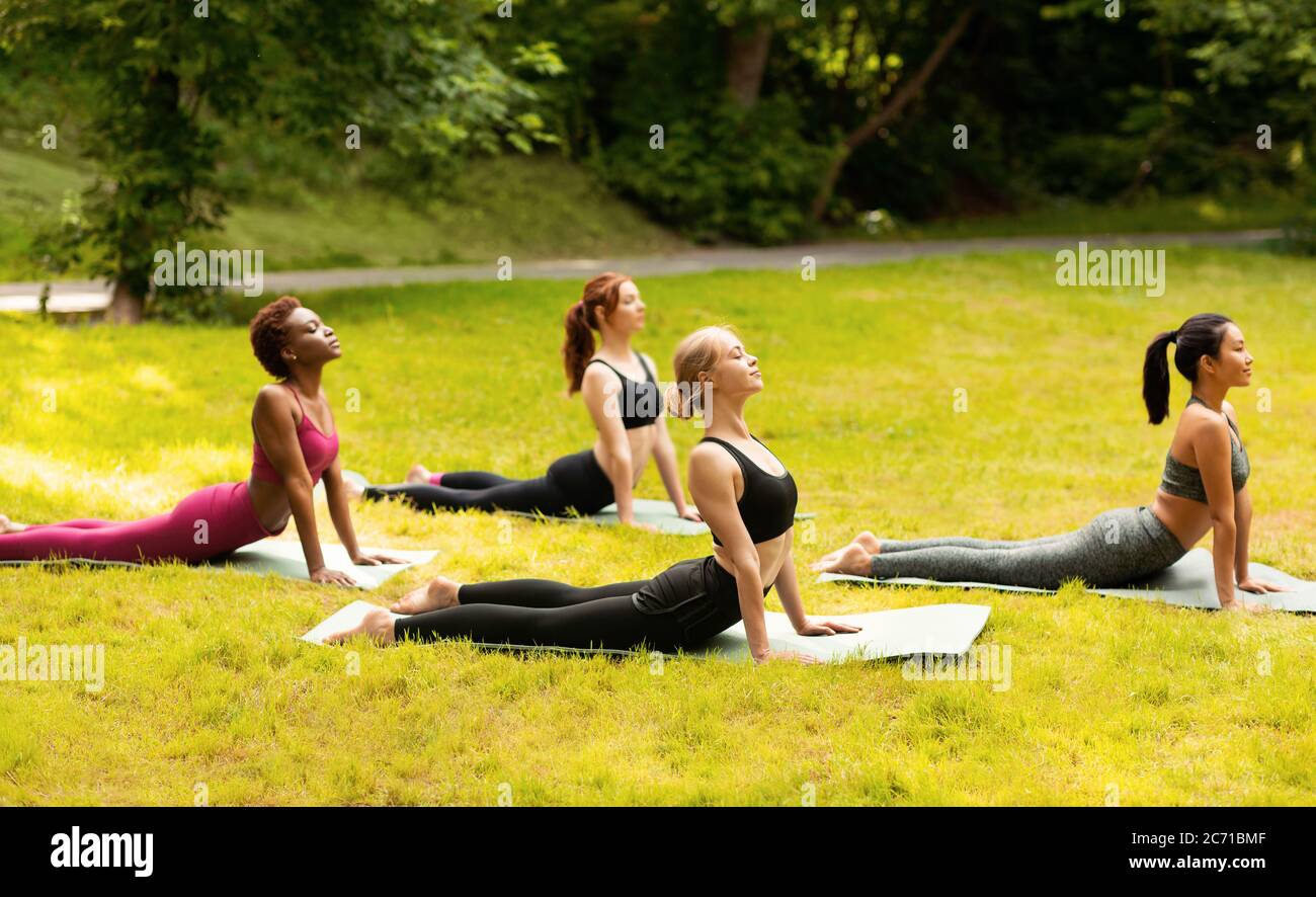 Groupe de filles diverses faisant le cobra yoga pose sur leur entraînement matinal au parc vert Banque D'Images